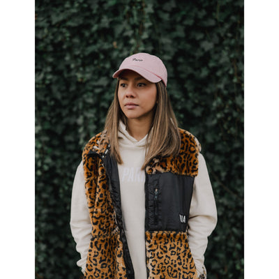 Person wearing a leopard print vest and pink cap against a green hedge background
