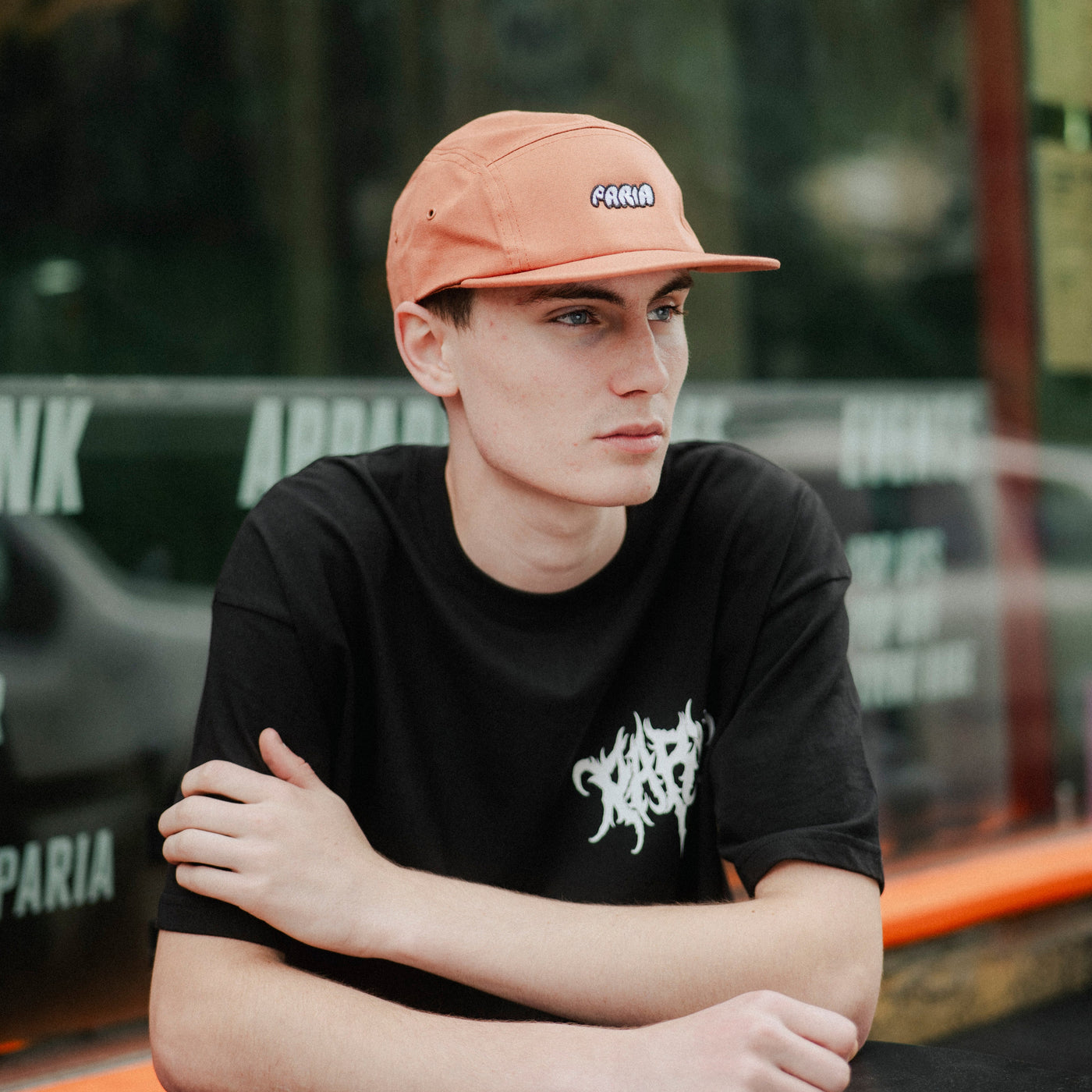model in black T-shirt with distressed paria logo and orange cap
