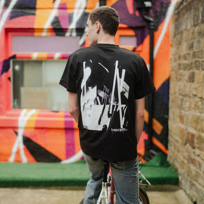 Person on a bicycle wearing a black t-shirt with white graphics in front of a colorful mural.