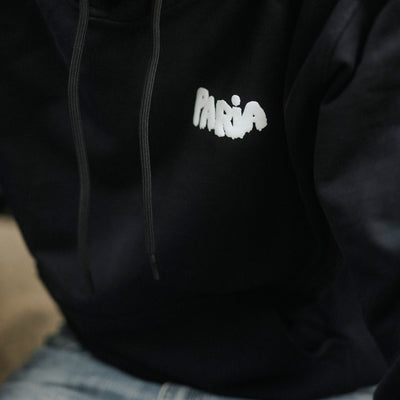 Person wearing a black hoodie with 'Paria' embroidered on it, blurred background