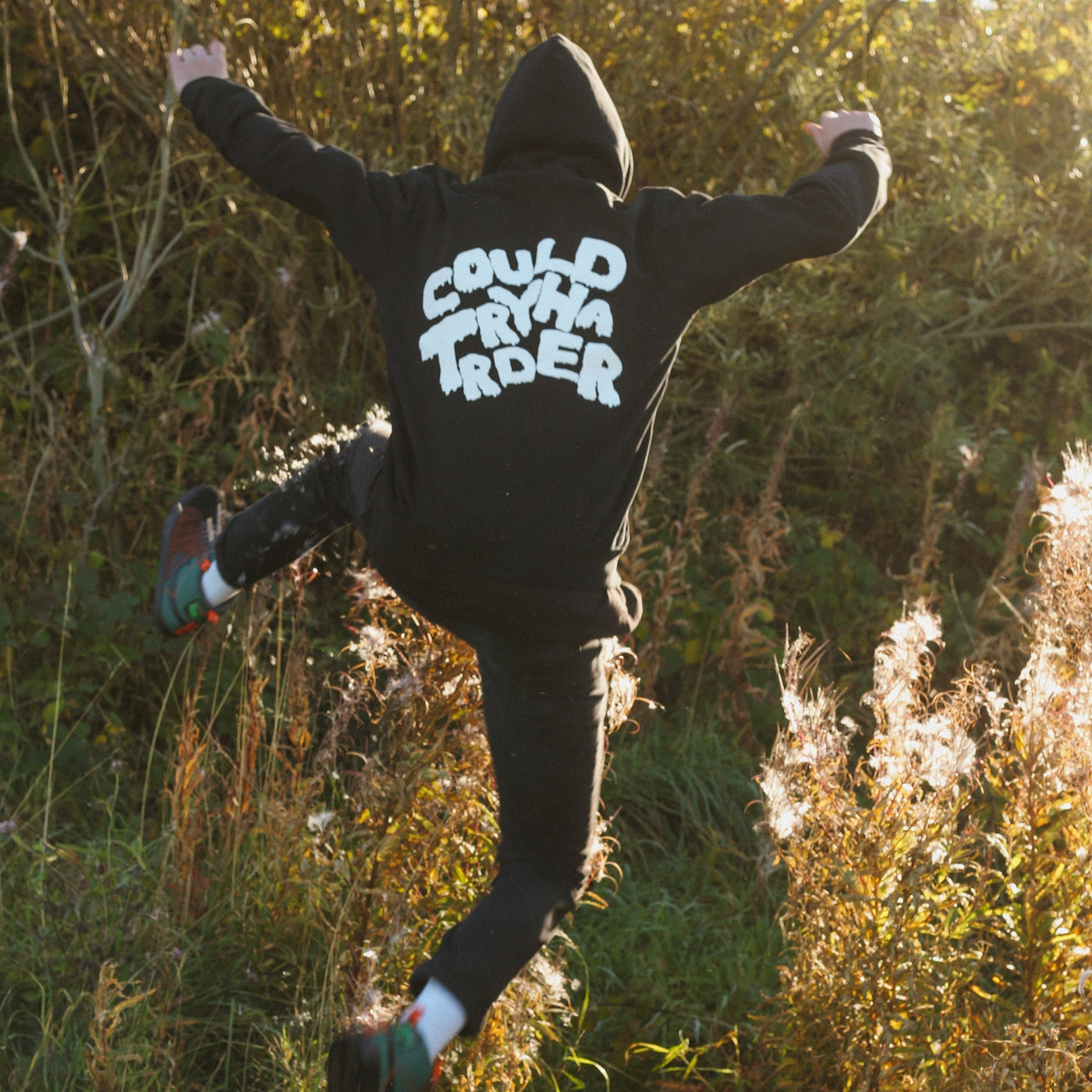 Person wearing a hoodie with text, jumping in a natural setting