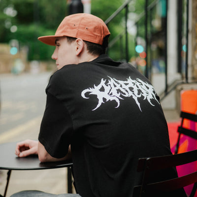 Person wearing a black T-shirt with white text sitting outdoors