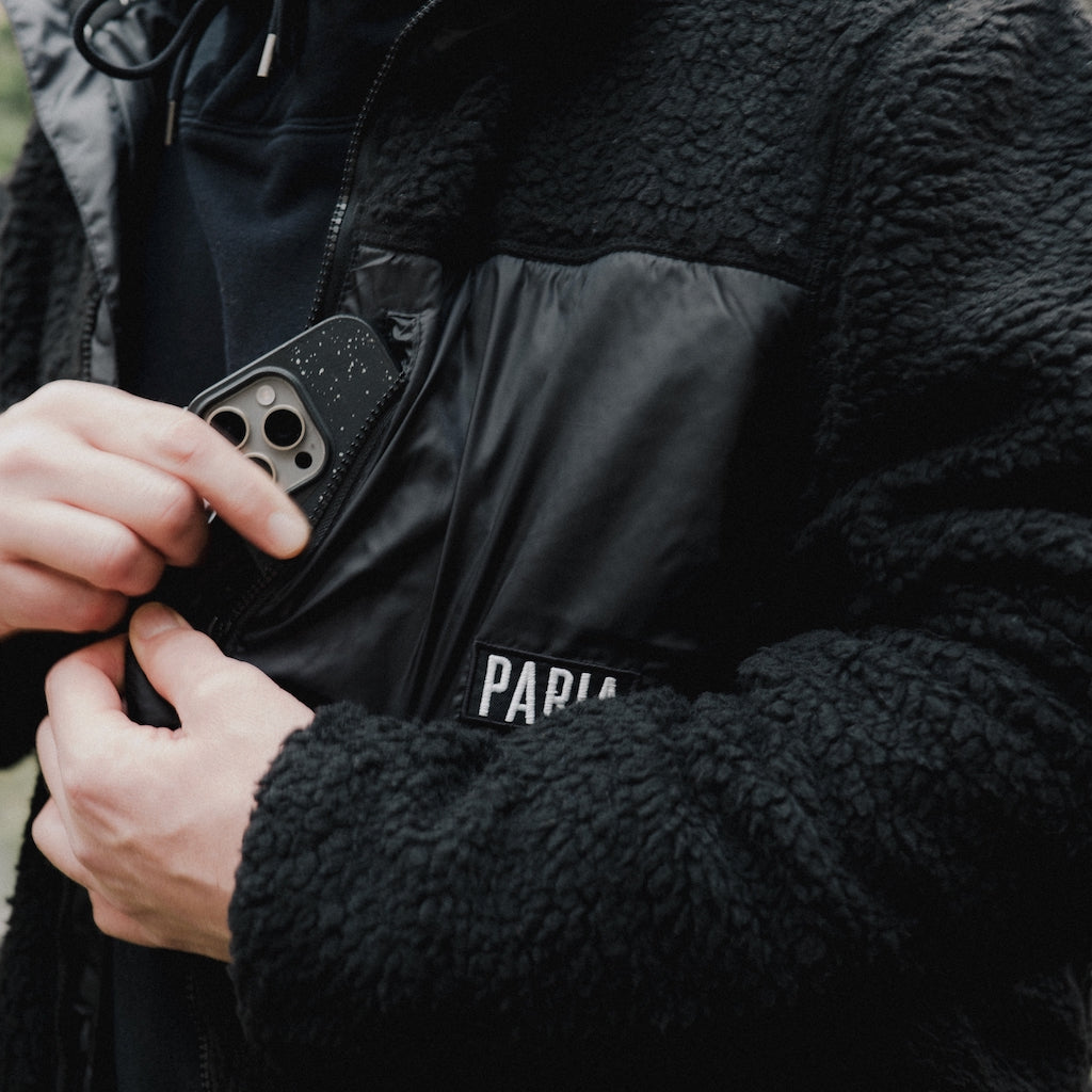 A black fleece cycling jacket with four zipped pockets and a logo on the upper left side, featuring a standing collar and zip front.