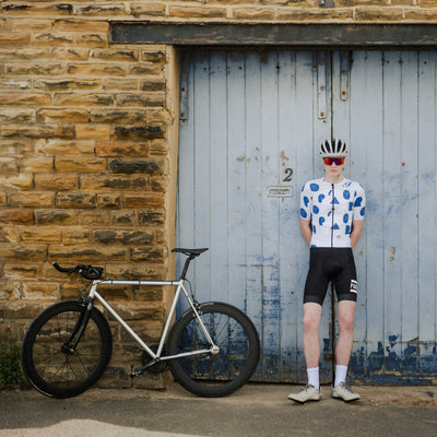 Person wearing a white cycling jersey with blue patterns, black shorts,