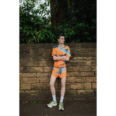 Person wearing a colorful outfit standing against a brick wall with greenery in the background