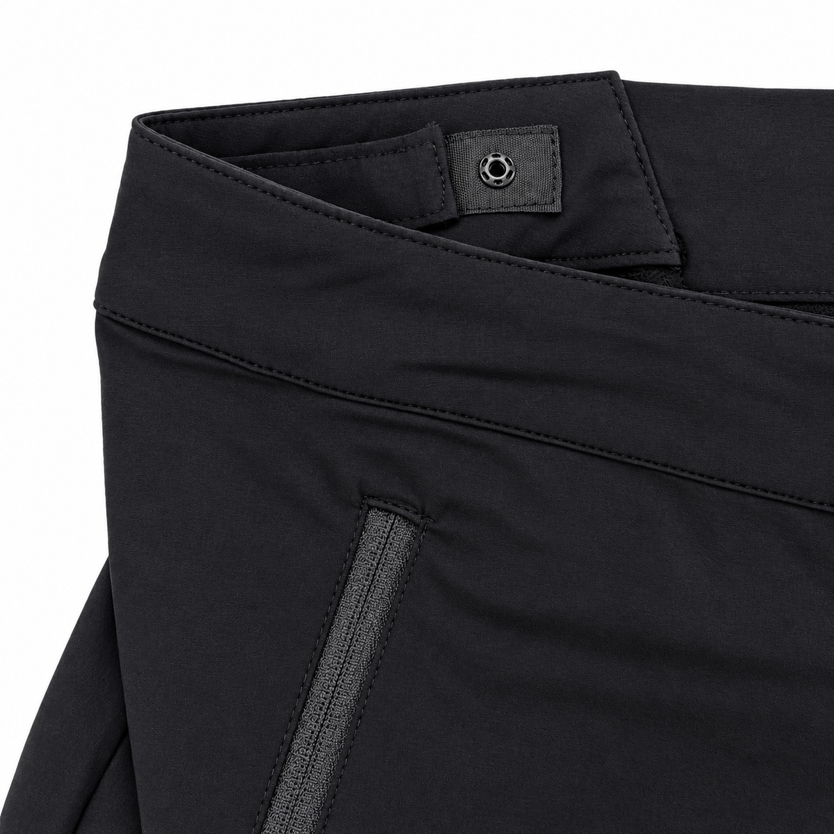 Close-up of black athletic pants showing the waistband, a small branded fabric tab, and a zippered pocket opening on a white background.
