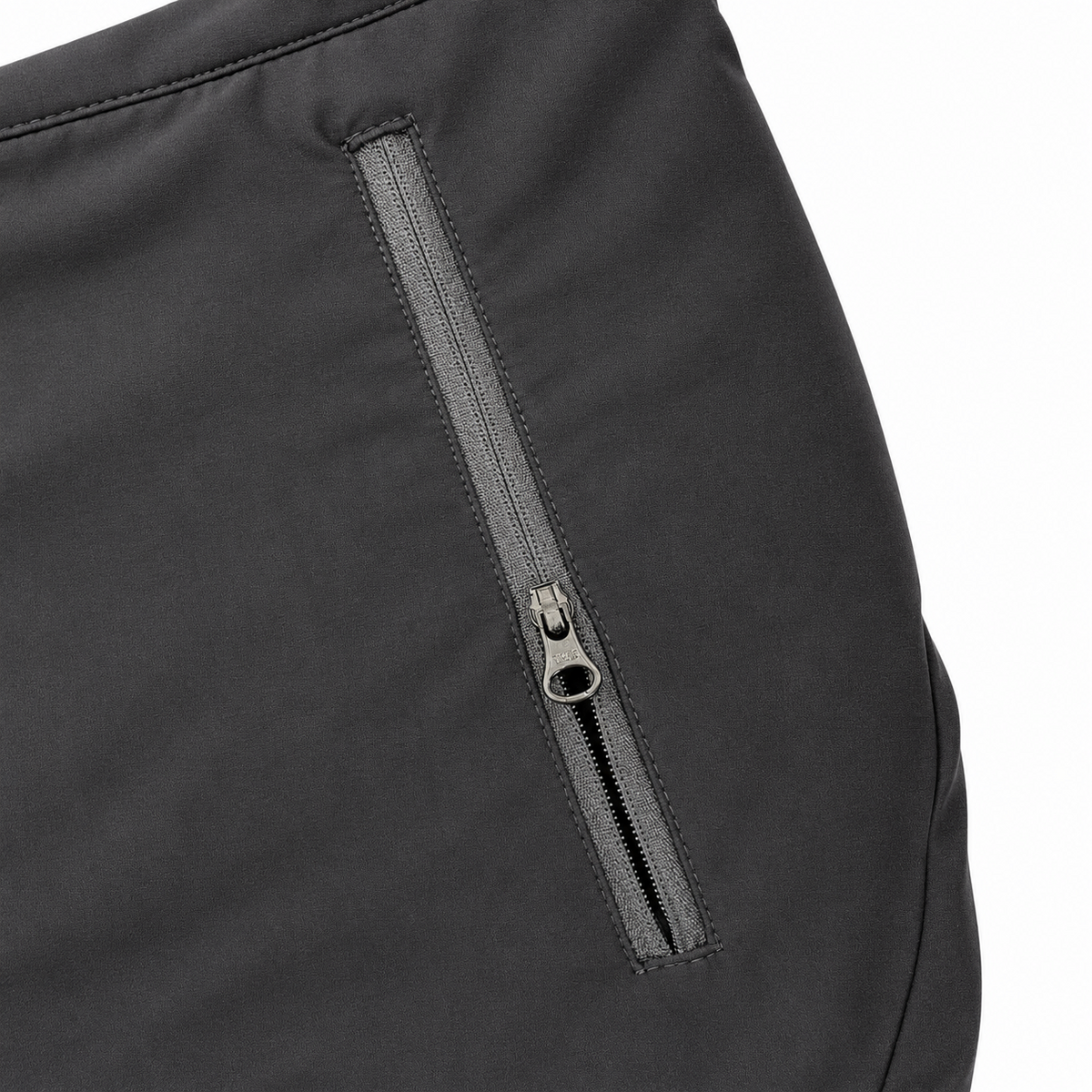 Close-up of a black softshell jacket showing a horizontal zippered pocket with a silver zipper pull on a white background.