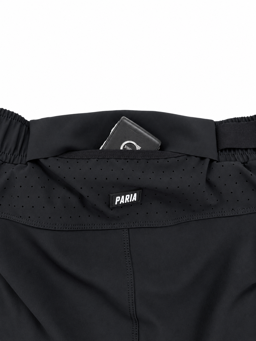 Close-up of the waistband of black athletic shorts, showing a perforated waistband panel, elastic waist, and a black brand label reading 'PARIA'.
