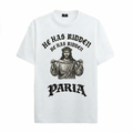 A white organic cotton t-shirt featuring a black woodcut-style graphic of Jesus Christ wearing a crown of thorns and holding a bicycle chain. Above the figure, the text reads "HE HAS RIDDEN" in a curved gothic font, with the PARIA brand logo in a matching black gothic typeface at the bottom.