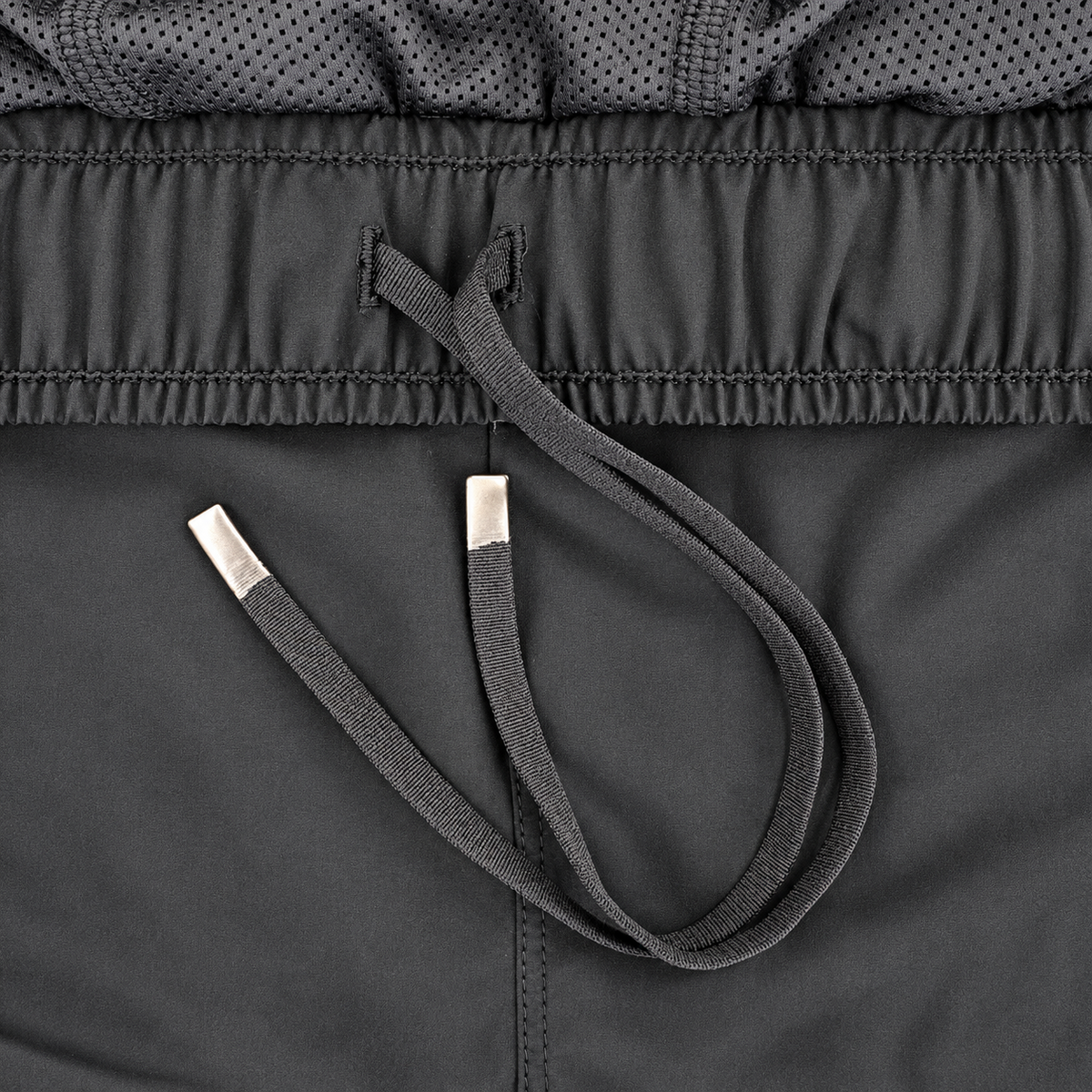 Close-up detail of a dark gray athletic garment showing the drawstring with silver metal tips, the elasticized waistband, and a perforated mesh fabric section.