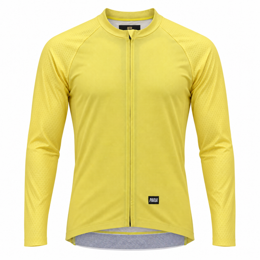 A yellow long-sleeve cycling jersey with a full-length front zipper, raglan sleeves, and a small black Paka logo patch near the bottom hem, shown on a plain white background.