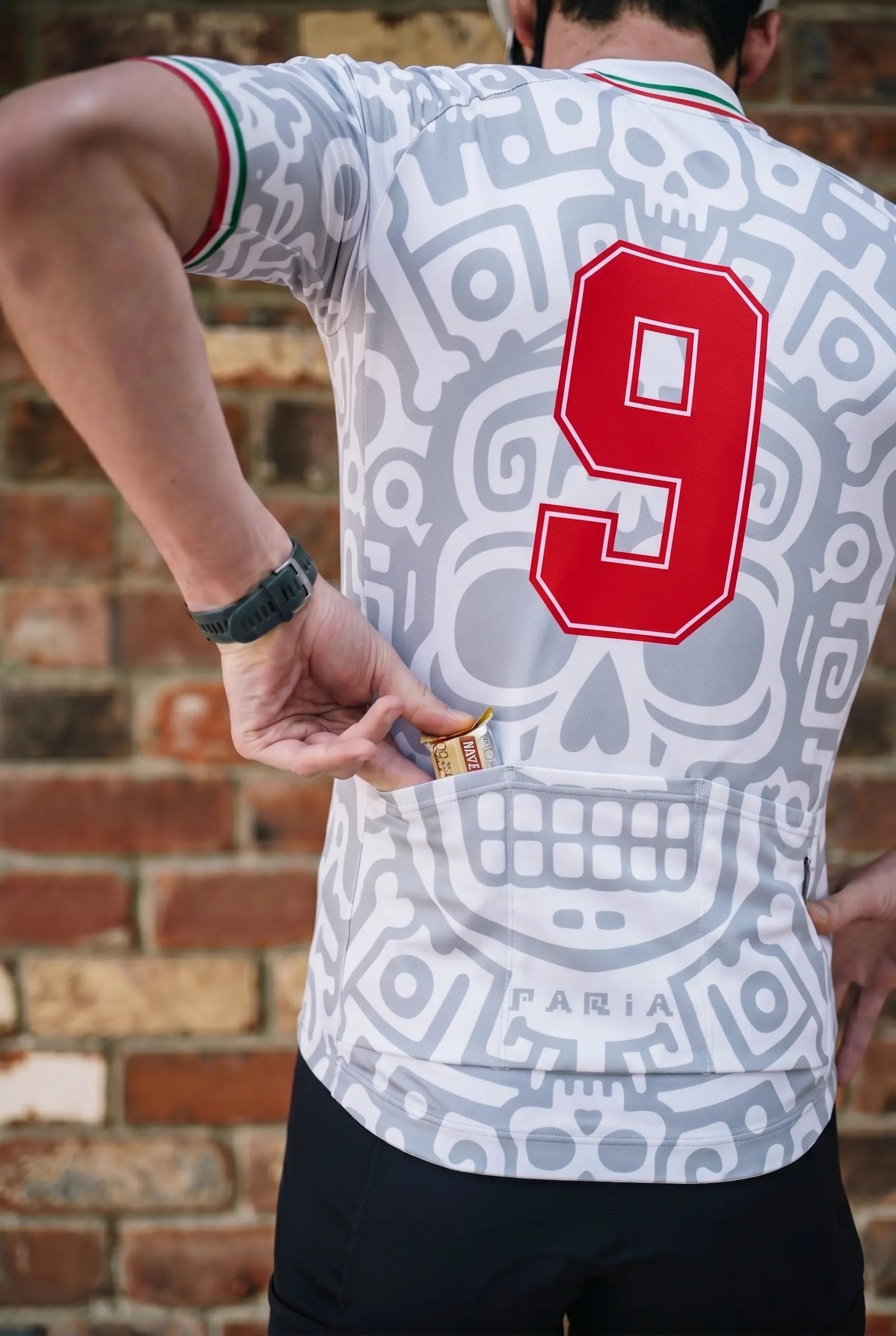 Person wearing a sports jersey with a red number 9 on the back, standing against a brick wall.
