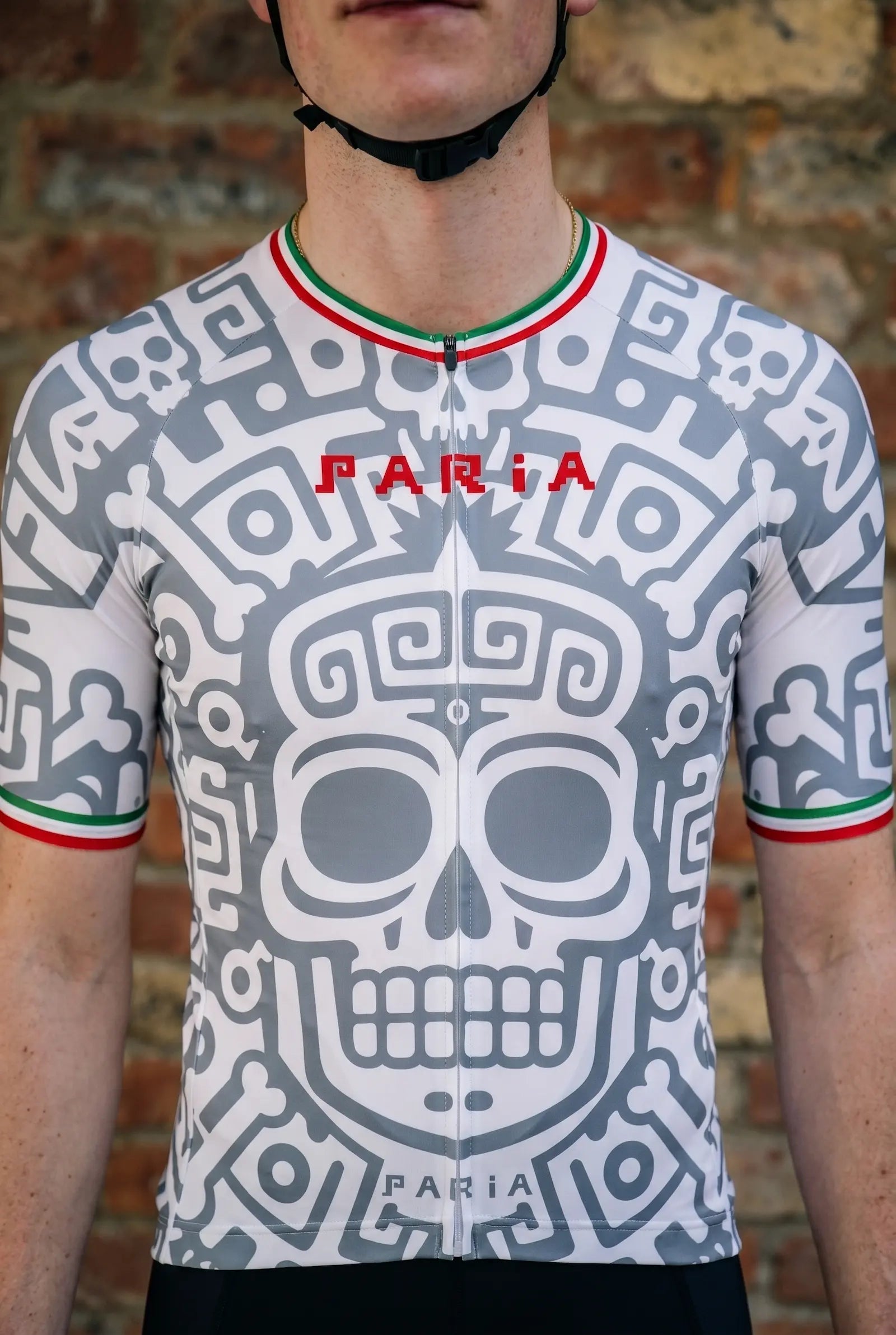 Person wearing a cycling jersey with a skull design and 'PARIA' branding against a brick wall.