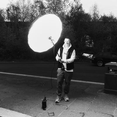 Person wearing sherpa gilet holding a large satellite dish outdoors with trees in the background