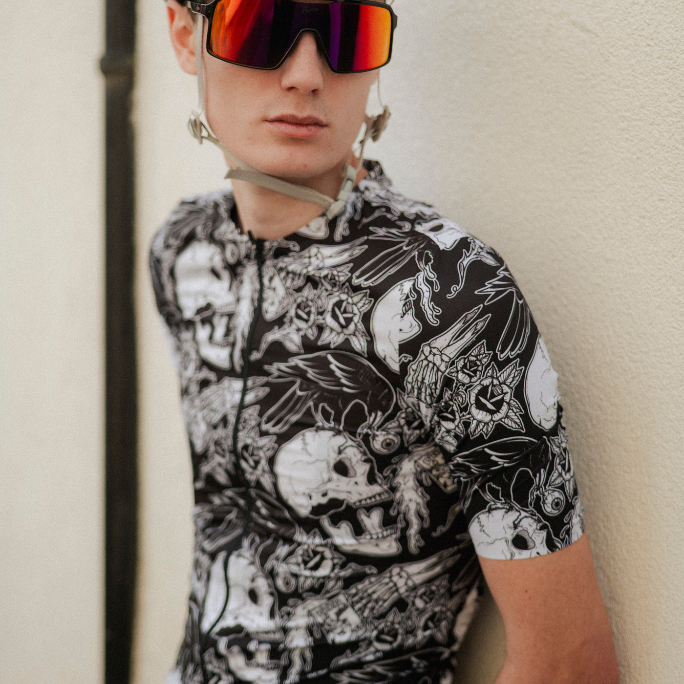 Person wearing a patterned cycling jersey and helmet with reflective sunglasses against a neutral background
